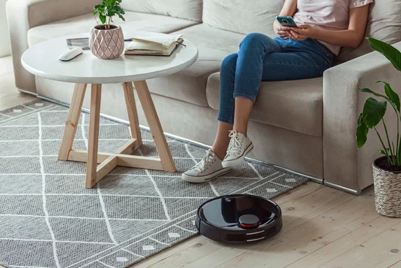 Person sitzt auf Sofa, während Saugroboter reinigt